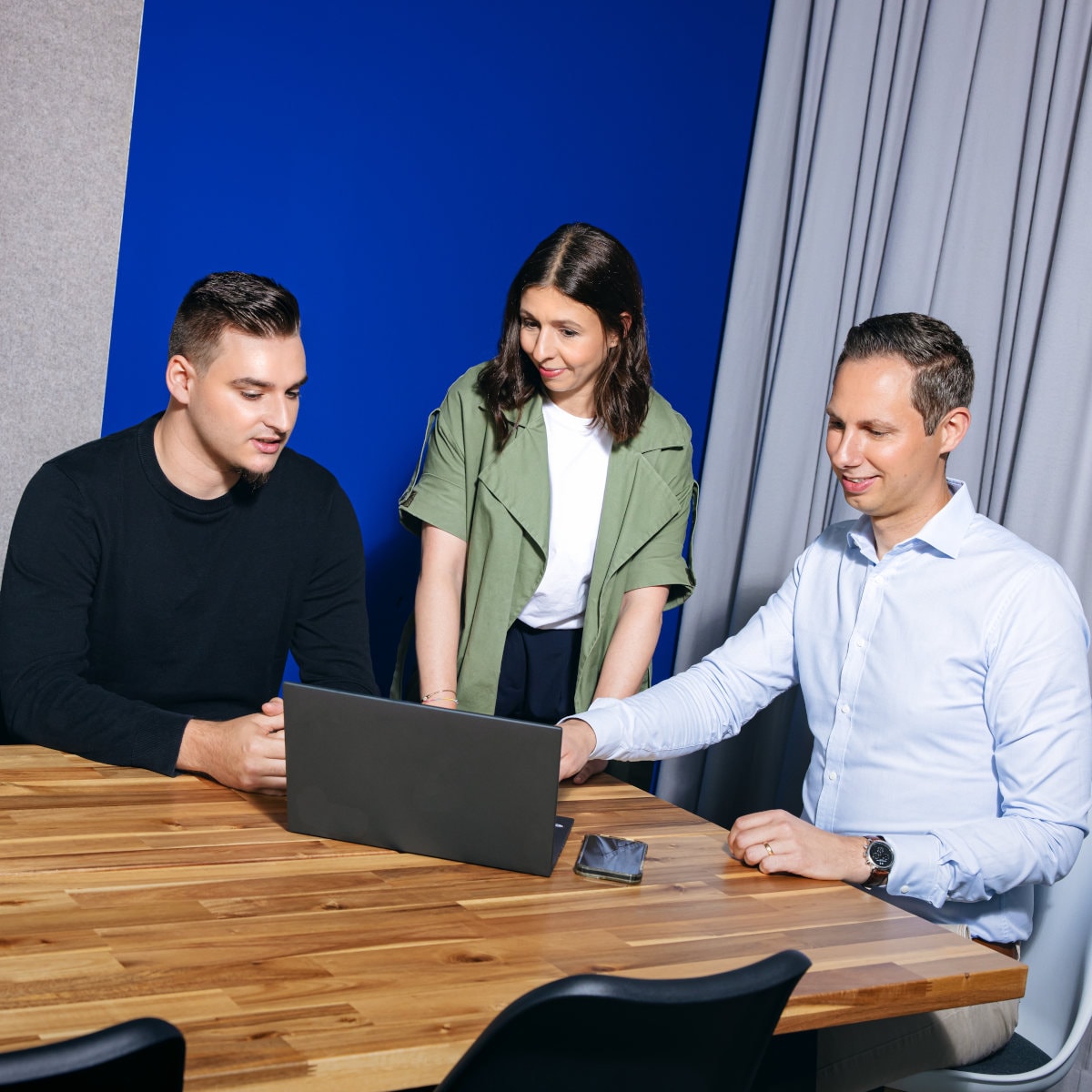 Three team members collaborating at a conference table, reviewing information on a laptop during a meeting