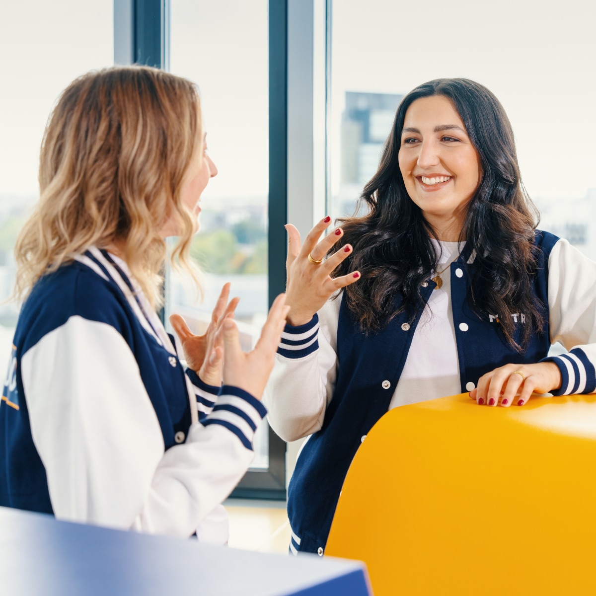 Two colleagues engaged in a conversation across a modern office seating area with bright yellow furniture