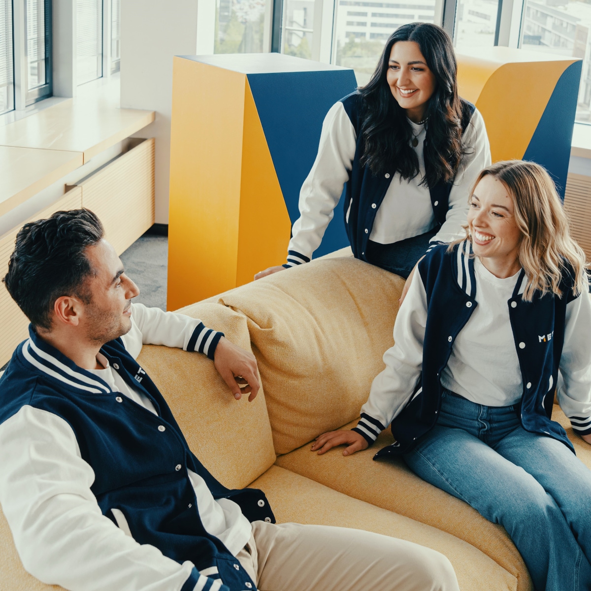 Three colleagues seated in a modern office lounge area having an informal discussion near large windows