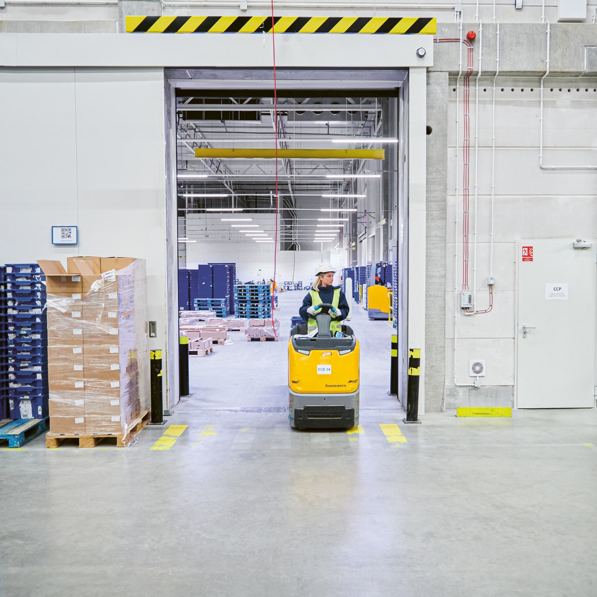 Warehouse aisle with stacked pallets, storage racks, and a yellow forklift operating in a large distribution center